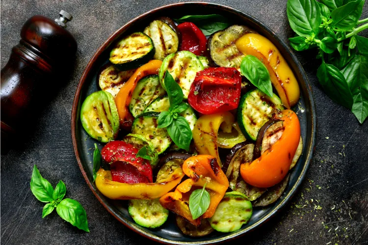 Assorted seasonal vegetables including squash, leafy greens, tomatoes, and herbs laid out on linen